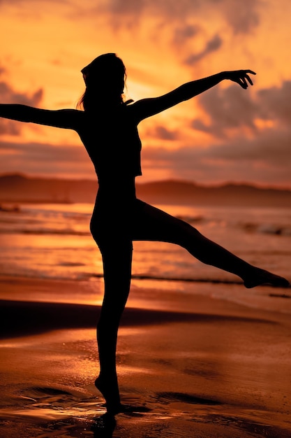 Eine Ballerina mit Silhouettenform führt am Strand bei brechenden Wellen sehr flexibel Ballettbewegungen aus