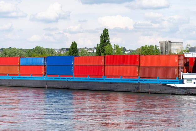 Foto eine barke mit vielen containern auf dem rhein in westdeutschland bäume und gebäude im hintergrund