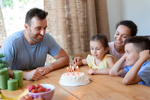 Eine befreundete Familie feiert zu Hause den sechsten Geburtstag eines kleinen Mädchens. Das Geburtstagskind bereitet sich darauf vor, die Geburtstagskerzen auf dem Kuchen auszublasen.