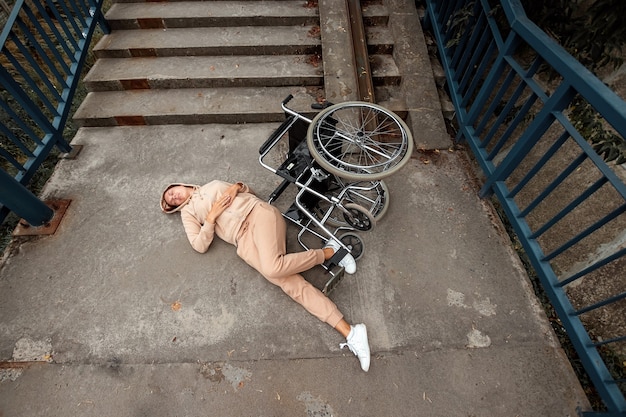 Eine behinderte Frau liegt auf dem Boden neben der Treppe neben dem Rollstuhl. Das Konzept eines Rollstuhls, einer behinderten Person, eines vollen Lebens, einer gelähmten, einer behinderten Person.