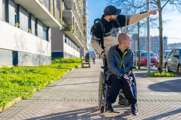 Eine behinderte Person im Rollstuhl, die mit einem Freund auf einem Stuhl auf der Straße spazieren geht