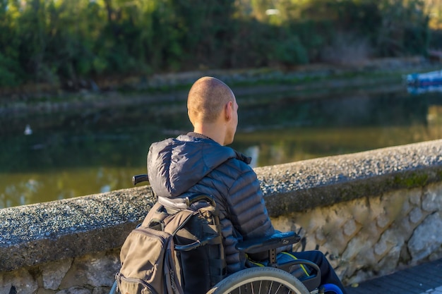 Eine behinderte Person im Rollstuhl in einem Park bei Sonnenuntergang neben einem Fluss