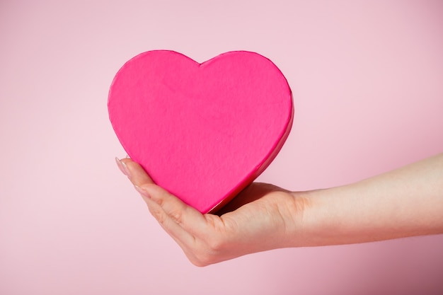 Eine Überraschung zum Valentinstag. Herzförmige Geschenkbox in der Hand der Frau. Platz für Ihren Text.