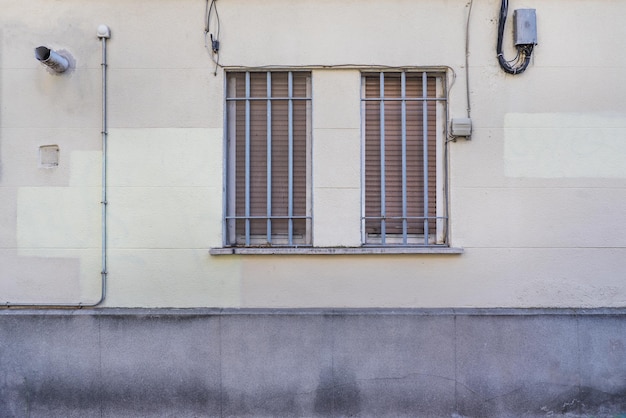 Eine Betonwand mit einem Doppelfenster mit einem grau gestrichenen Kreuzgitter