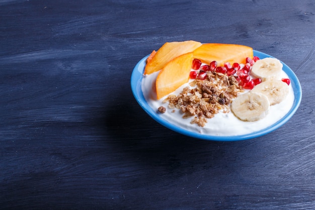 Eine blaue Platte mit griechischem Joghurtgranola-Persimonebananengranatapfel auf schwarzem Hintergrund