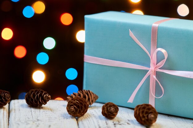 Eine blaue Weihnachts- oder Neujahrsgeschenkbox mit rosa Band auf Holzoberfläche gegen bunte Lichter