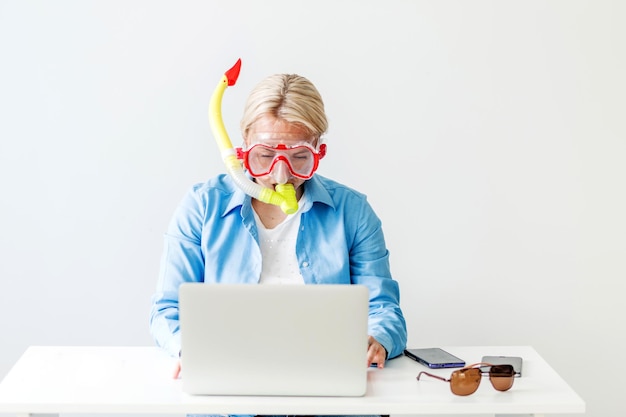 Eine blonde Frau in einer Taucherbrille sitzt im Büro und bestellt Online-Tickets für eine Touristenreise für einen Flugzeugbus oder Zug Frau träumt vom Meer am Arbeitsplatz Horizontales Foto