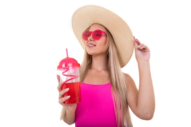 Eine blonde junge Frau in einem rosa Badeanzug und Hut trinkt Limonade