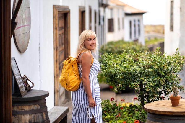 Eine Blondine im Sommerkleid mit Rucksack geht die Straße der Altstadt von Garachico auf der Insel Teneriffa entlang