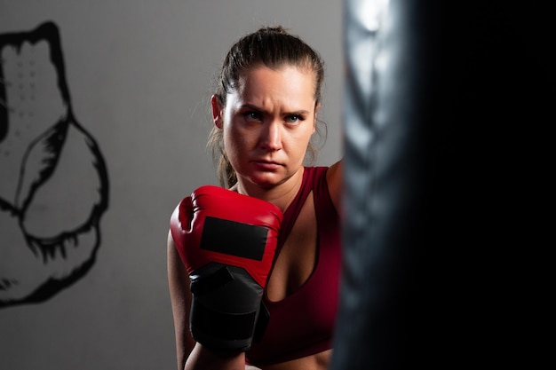 Eine Boxerin in einem roten Trainingsanzug schlägt auf einem dunklen Hintergrund auf einen Boxsack