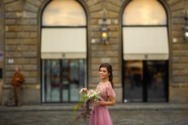 Eine Braut in einem rosa Kleid mit einem Blumenstrauß steht im Zentrum der Altstadt von Florenz in Italien