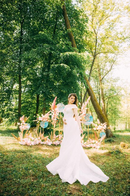 Eine Braut in einem traditionellen weißen Kleid mit einem Hochzeitsblumenstrauß neben dem Hochzeitsbogen