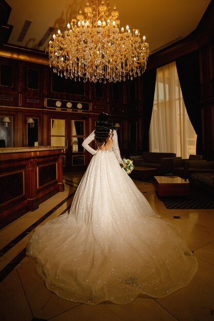 Eine Braut in einem weißen langen Kleid mit einem Bouquet in den Händen steht