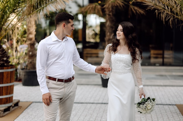 Eine Braut und ein Bräutigam gehen Hand in Hand, der Bräutigam trägt ein weißes Kleid mit Spitzenärmeln.