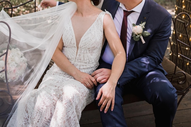 Eine Braut und ein Bräutigam sitzen auf einer Bank und halten die Hände mit dem Schleier der Braut.