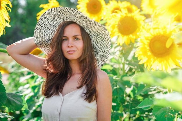 Eine brünette Frau mit Hut steht in einem Sonnenblumenfeld