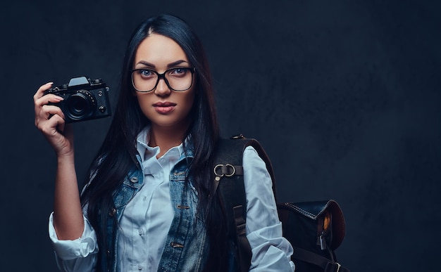 Eine brünette Reisende mit Rucksack hält eine kompakte Fotokamera.