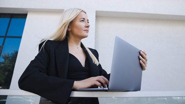 Eine Business-Lady im stylischen Anzug arbeitet auf der Straße an einem Laptop