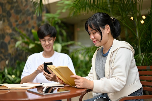 Eine College-Studentin liest ein Buch, während ihr männlicher Freund ein Smartphone benutzt