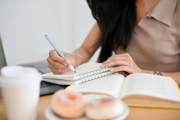 Eine College-Studentin sitzt im Café und macht ihre Hausaufgaben und schreibt auf ihr Notizbuch