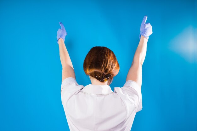 Eine Dame in medizinischer Uniform und Handschuhen hält ihre Hände auf blauem Hintergrund hoch