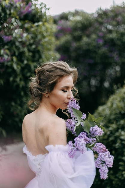 Eine delikate, elegante junge Braut in einem Hochzeitskleid geht in einem blühenden Frühlingspark im Freien spazieren
