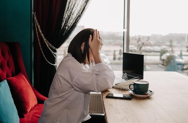 Eine depressive Geschäftsfrau sitzt mit Laptop und Papieren an einem Tisch in einem Café