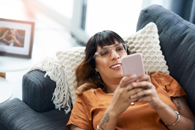 Eine der vielen Social-Media-Apps auswählen, um die Langeweile zu vertreiben Schnappschuss einer jungen Frau, die ihr Handy benutzt, während sie sich zu Hause auf dem Sofa entspannt