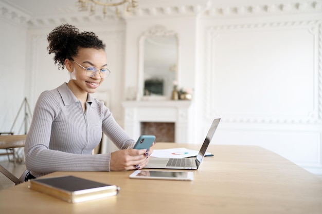 Eine Designerin mit Brille arbeitet im Büro an einem neuen Projekt in einem Finanzunternehmen mit einem Laptop auf dem Tisch und einem Telefon