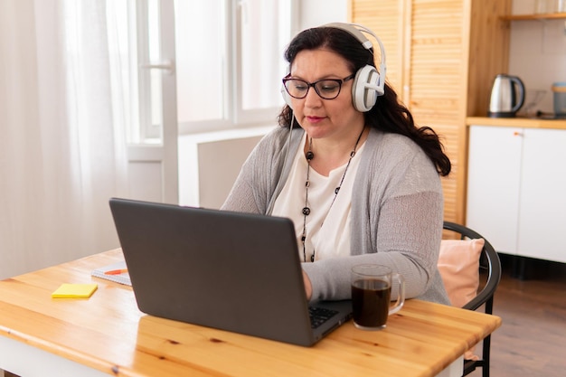 Eine dicke Frau sitzt mit einem Laptop an einem Tisch. Sie nimmt Bestellungen mit Kopfhörern auf. Sie ist in der Küche.