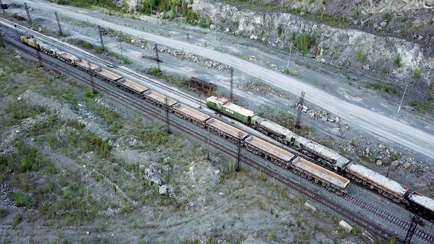 Eine Diesellokomotive schiebt einen mit Schutt gefüllten Müllwagen im Hintergrund eines Steinbruchs