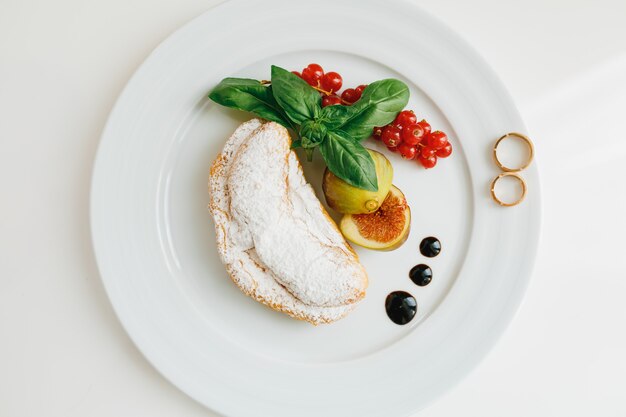 Eine Draufsicht auf einen Teller mit zwei goldenen Eheringen, einem Croissant mit Puderzucker und Feigen und