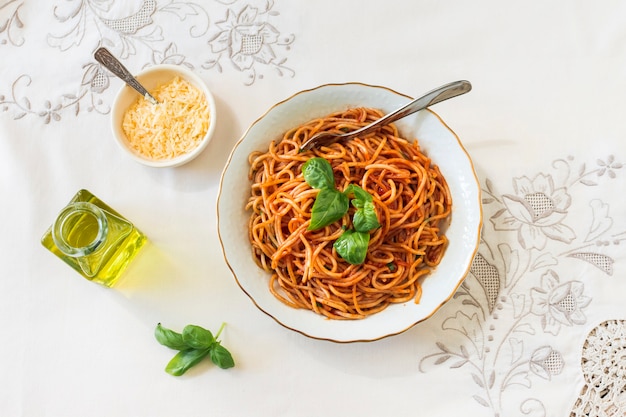 Eine Draufsicht auf Spaghetti mit Käseschüssel; Basilikum und Olivenöl auf Tischdecke