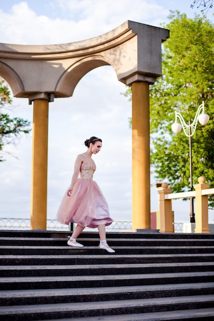 Eine dünne weibliche Ballerina in einem rosa Seidenkleid und Spitzenschuhen mit Schleifen fällt anmutig nach unten ...