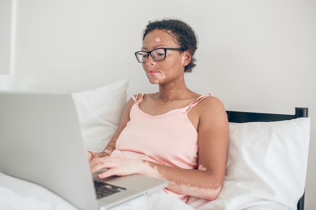 Eine dunkelhäutige Frau, die im Bett auf einem Laptop tippt