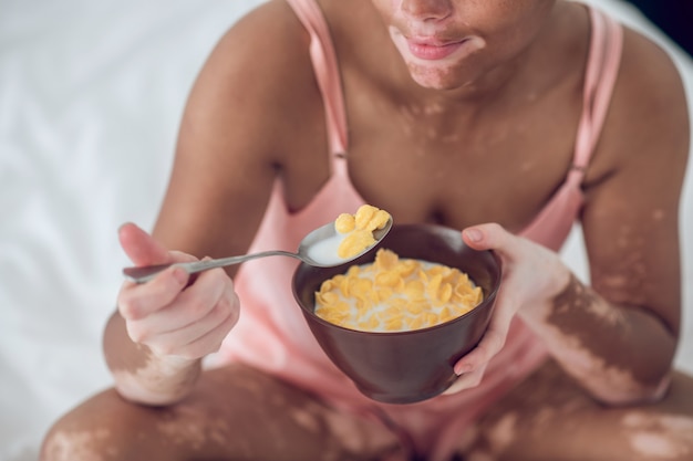 Eine dunkelhäutige Frau isst Müsli, während sie auf dem Bett sitzt