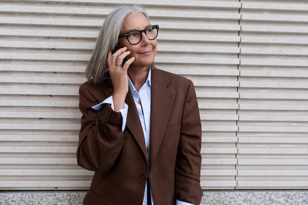 Eine einjährige, erfolgreiche kaukasische Geschäftsfrau in einem braunen, eleganten Anzug spricht auf einem Smartphone