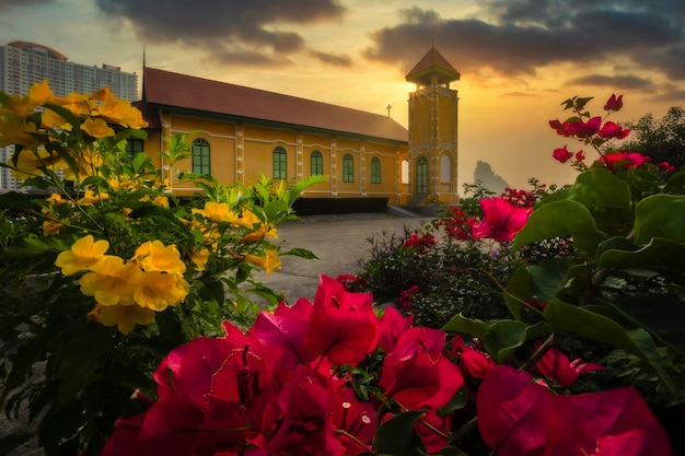 Eine einsame Holzkirche in der Abenddämmerung mit Sonnenuntergangswolken und schönen Blumen im Vordergrund.