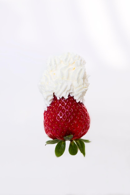 Eine einzelne Erdbeere auf weißem Hintergrund mit Schlagsahne an der Spitze