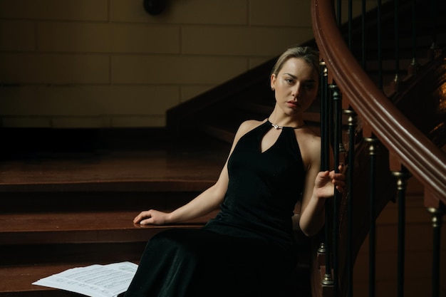 Foto eine elegant luxuriöse blonde frau in schwarzem abendkleid sitzt auf der operntreppe mit notenmusik