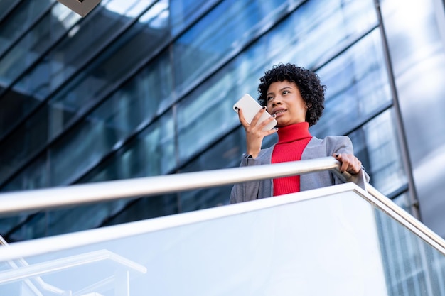 Eine elegante afroamerikanische Frau mit dem Telefon in einem Bürogebäude bei der Arbeit