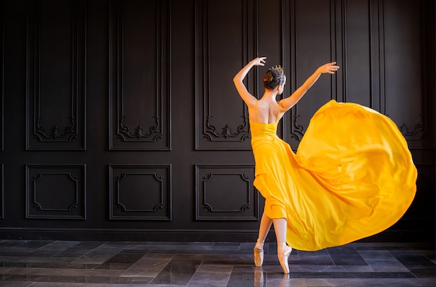 Eine elegante Ballerina in Spitzenschuhen tanzt mit einem fließenden gelben Stoff auf einem dunkelgrauen Hintergrund