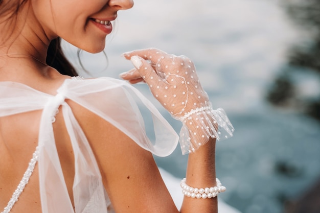 Eine elegante Braut in einem weißen Kleid, Handschuhen und nackten Füßen sitzt in der Nähe eines Wasserfalls im Park und genießt die Natur. Ein Modell in einem Hochzeitskleid und Handschuhen in einem Naturpark. Belarus.