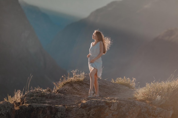 Eine elegante Frau in einem Sommerkleid posiert sanft genau zwischen den malerischen, weitläufigen Felsbergen