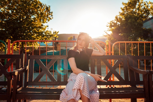 Eine elegante Frau wartet auf einer Parkbank im Hintergrund auf einen sonnigen Sommerurlaub bei Sonnenuntergang