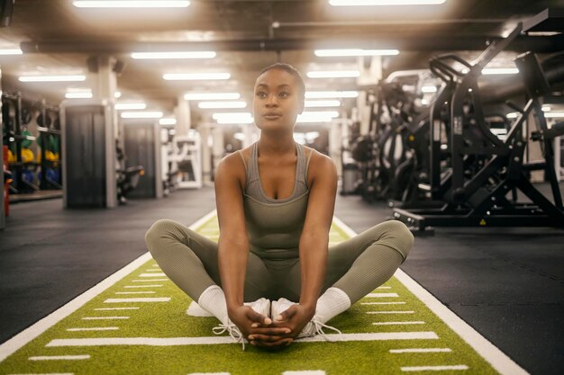 Eine engagierte, fitte schwarze Sportlerin sitzt auf dem Fitnessboden und streckt ihre Beine