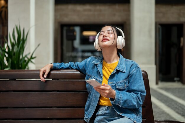 Eine entspannte Frau genießt die Musik mit ihren Kopfhörern, während sie auf einer Bank in der Stadt sitzt