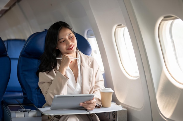 Eine erfolgreiche asiatische Geschäftsfrau sitzt mit ihrem digitalen Tablet am Fenster in einem Flugzeug