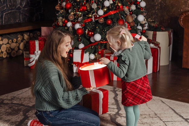 Eine erfreute Mutter und ihre Tochter öffnen eine große Geschenkkiste und schauen hinein Familienabend Weihnachtsbaum im Hintergrund