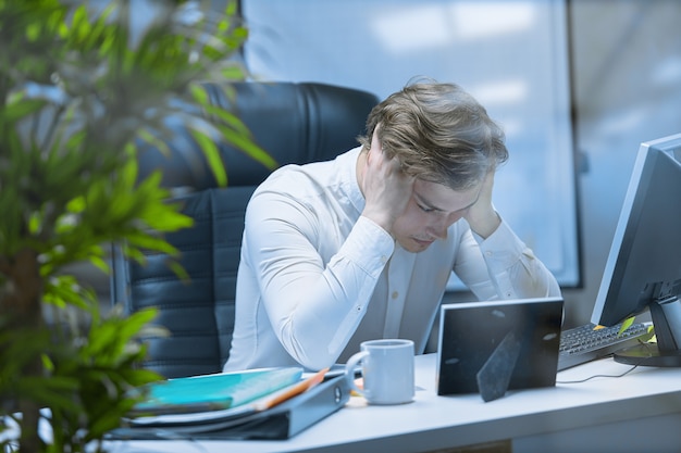 Eine erschöpfte Person am Arbeitsplatz nach einem harten Arbeitstag, müde von der Routine.